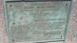 A bronze memorial plaque mounted on stone honors Colonel Israel Angell, featuring an engraved tribute letter from George Washington.