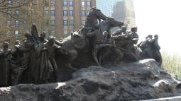 A large bronze monument shows soldiers and civilians in dramatic motion, with horses and figures emerging from a rugged base in an outdoor urban park.