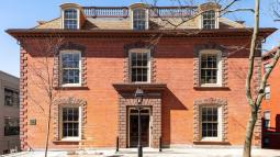 A three‑story brick brownstone building with symmetrical windows and a central stone‑framed entrance stands behind a black streetlamp.