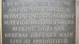 A bronze plaque mounted on a stone surface commemorates a June 23, 1780 battle where Americans delayed advancing British forces near Springfield.