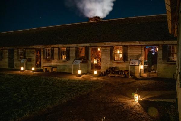 Candles in lanterns pour a golden light onto a darkened wooden building.