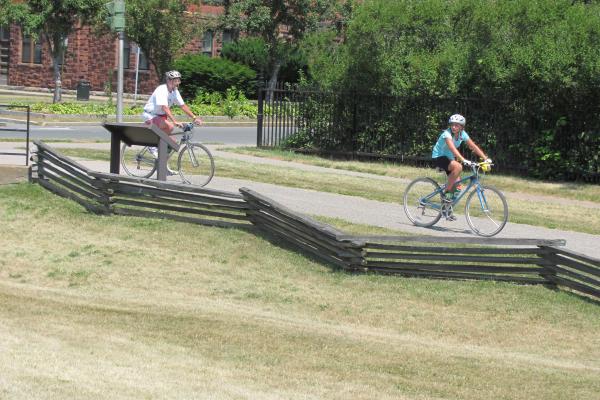 Two people cycle in a line down the park trail.