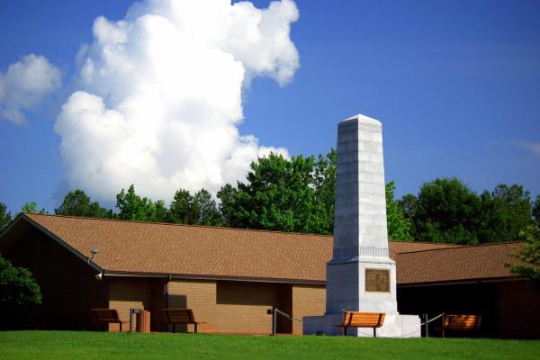 US Monument stands in front of visitor center. White cloud in deep blue sky is above them.