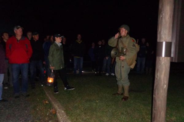 Man in WW II military uniform leading group of visitors holding lanterns