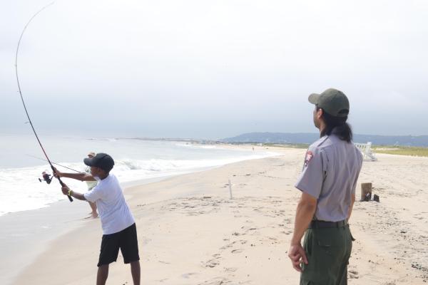 Child casting fishing rod being watched by park ranger