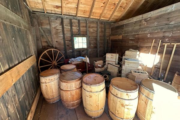 Barrels and boxes of 18th century military supplies stacked inside of a barn.
