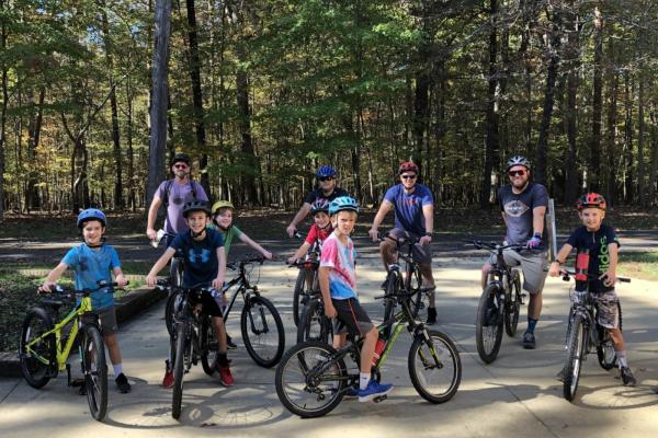 Ten men and boy cyclists pose with their road bikes, wearing helmets and smiling