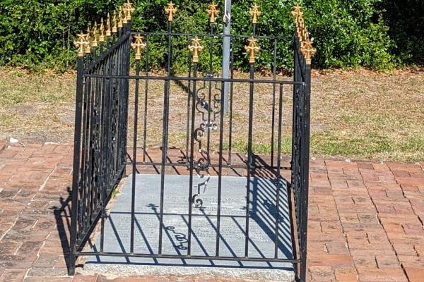 Image of an in ground tombstone with black and gold fencing surrounding