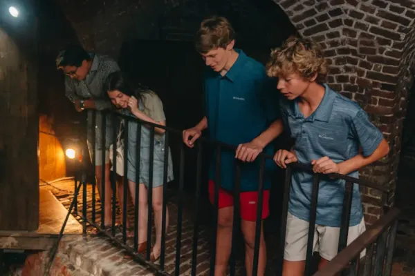 2 boys, a girl and a woman looking over a railing in a dungeon during a ghost tour