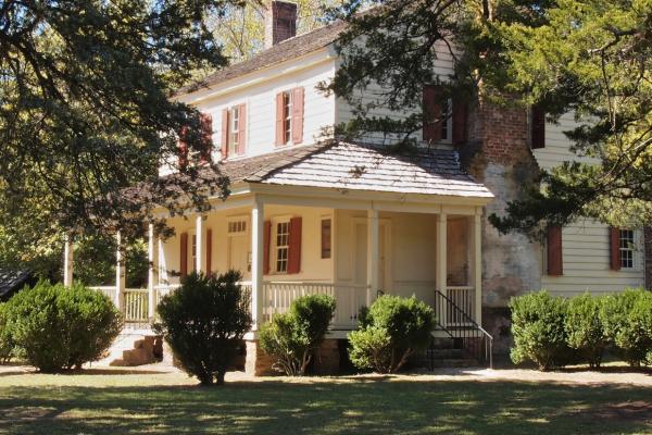 Image of a large colonial house partially hidden by pine trees