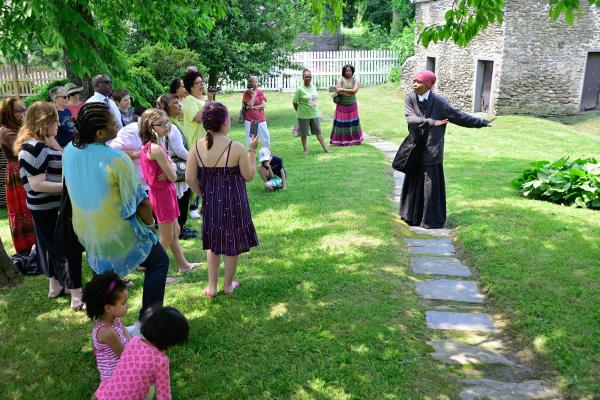 A costumed woman speaks in front of a group of tourists outside