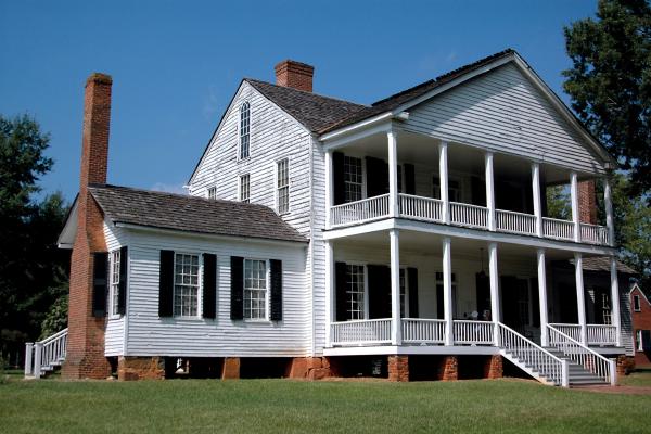 A photo of a large white colonial era three story house with columns