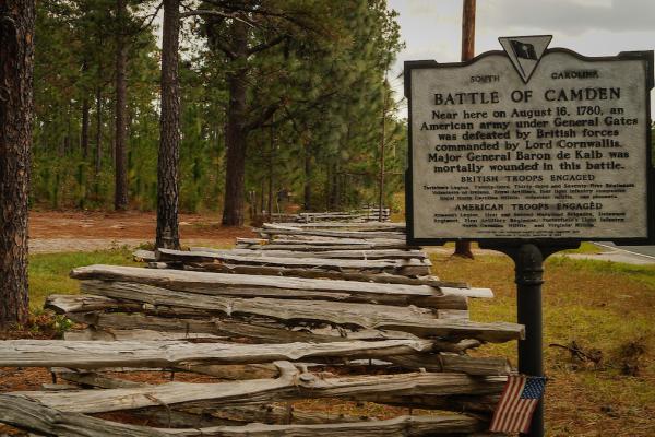 Image of a split rail fence along the side of a road with a historical marker sign reading Battle of Camden