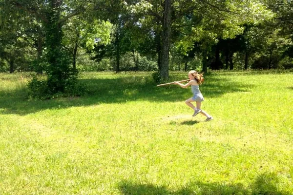 a little girl running through a field with a toy musket