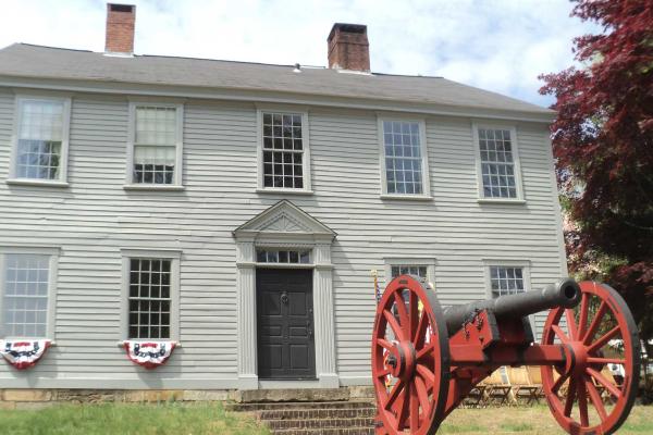 Facade of the two story Nathanael Greene homestead with an artillery piece in the foreground