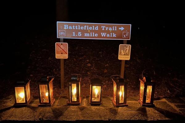 6 lanterns are shining in the night in front of a sign that says "Battlefiield Trail 1.5mi walk"