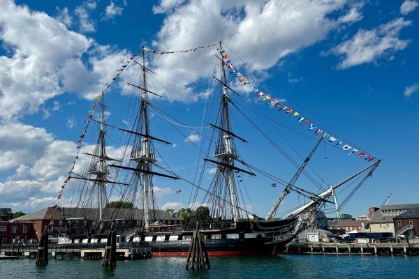 USS Constitution, a three-masted sailing ship, is decorated in flags on a partly-cloudy day.