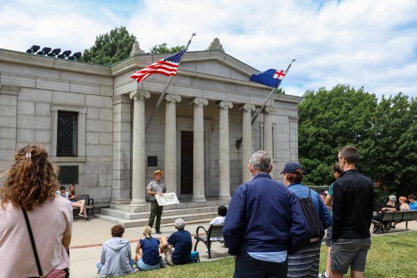 A ranger stands in front of the Bunker Hill Lodge speaking to a group of people