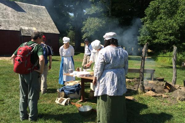 Women in colonial clothing giving a demonstration to tourists.