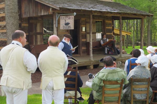 Reenactors listen as another reenactor presents and 18th century church service.