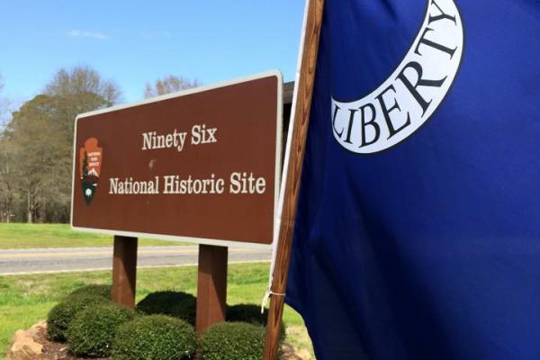 A blue Liberty flag is in the right foreground with the park entrance sign behind it.