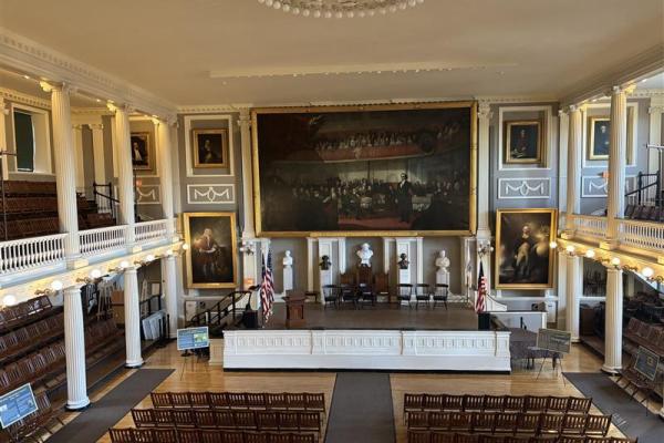 Photo of a big hall with a balcony, stairs on the floor, and artwork adorning the walls