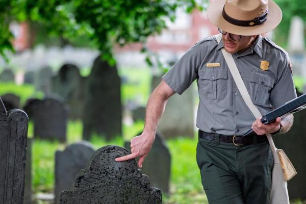 A park ranger pints out something on a historic 18th century gravestone