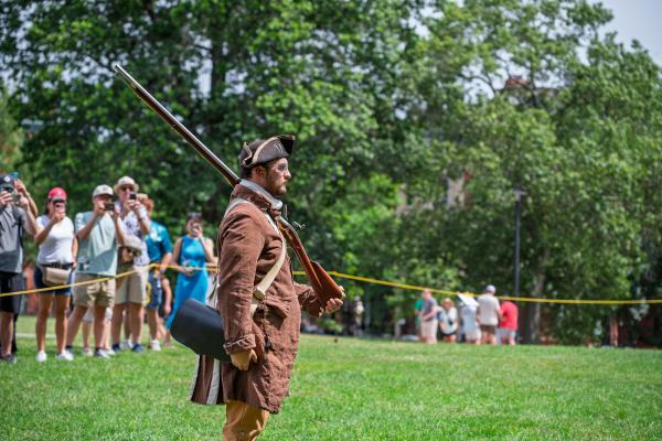 A ranger dressed in period clothing has a musket resting on his shoulder in front of an audience