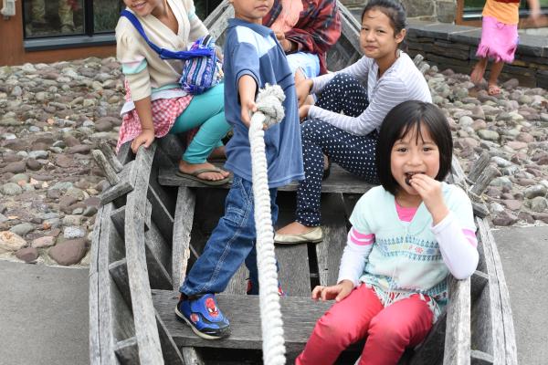 Several kids sit crowded together in a bateau-style boat.