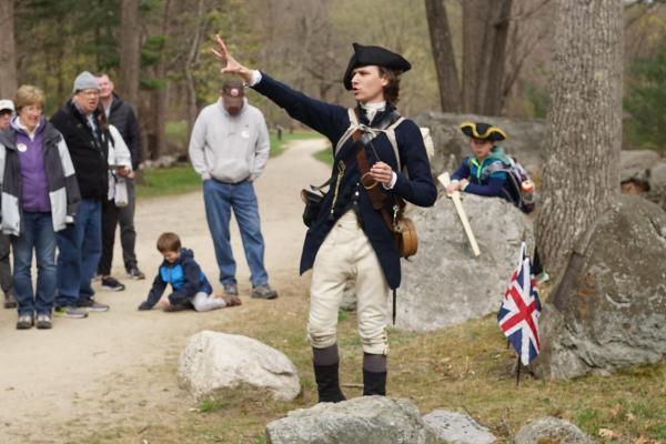 A Park Ranger in 18th Militia clothing stands in front of a crowd talking and pointing.