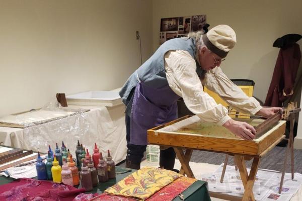 a man in colonial dress hand-coloring paper
