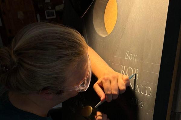 Michael Brache carving a gravestone with a chisel in dramatic low lighting