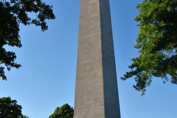 A crowd gathers on the lawn in front of the tall Bunker Hill Monument