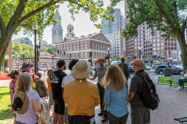 Visitors stand in front of a Ranger leading a tour, Faneuil Hall is in the background