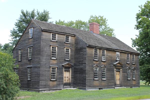 A wooden colonial era house with multiple stories and windows
