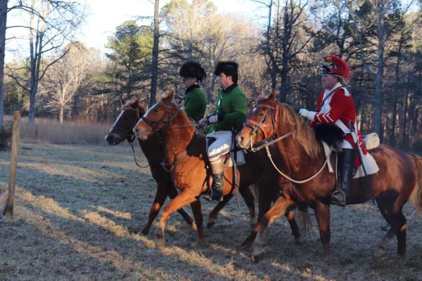 Three living historians in 18th century military uniforms ride horses