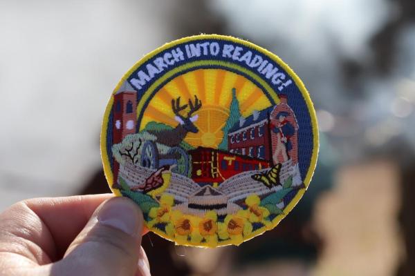 March Into Reading patch held up in front a smokey field caused by muskets being fired