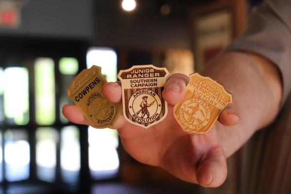 A hand holds out three junior ranger badges