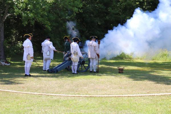 Group of living historians in white hunting frocks fire a cannon