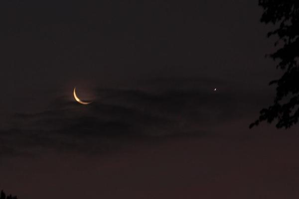 The crescent moon and Venus shine across from each other in a dark purple sky.