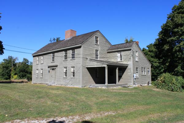 A wooden 18th century house sits in a field of green grass