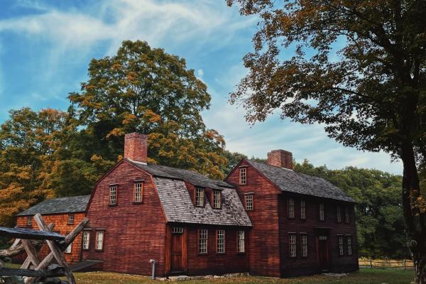 A wooden colonial era house surrounded by tall trees