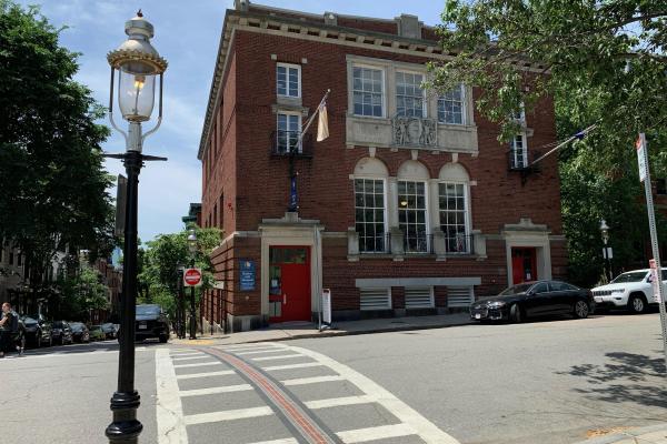Brick building on street corner with three arched windows in center.