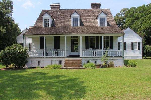 White 1-1/2 story wood house with porch extending across main house with brick stairs in the center