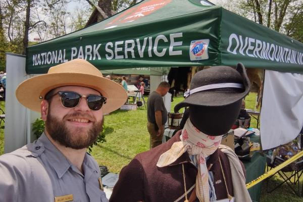 A park ranger with sunglasses poses beside a mannequin in historical clothing