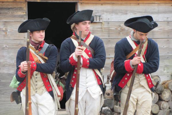 Three Continental Soldiers stand shoulder to shoulder in a relaxed stance, holding their muskets.