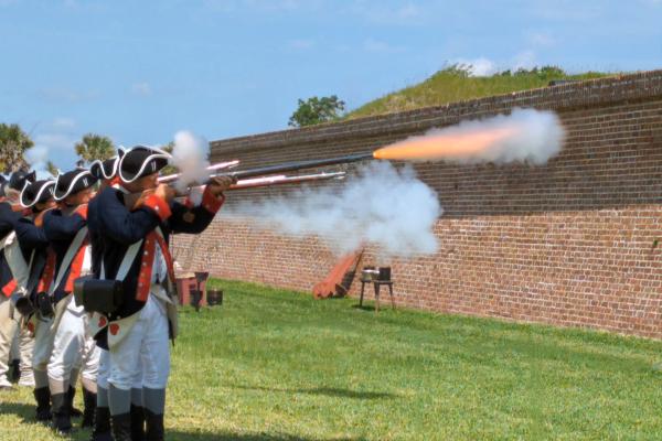 A row of living historians fire muskets during Carolina Day events