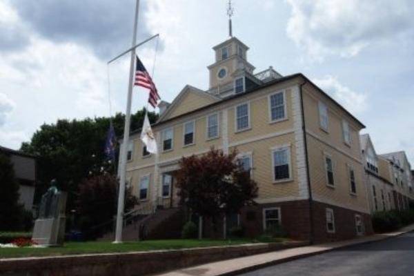 A historic yellow civic building stands behind a flagpole flying the American flag.