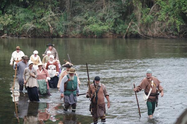 People in costumes walking through a river knee-deep.