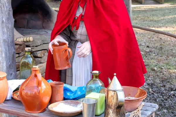 A woman in 18th century clothing is working with dishes.